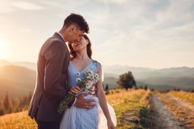 Genç, sevgi dolu bir çift gün batımında dağlarda sarılıyor. Yazın Karpatlar 'da mutlu gelin ve damadın portresi.