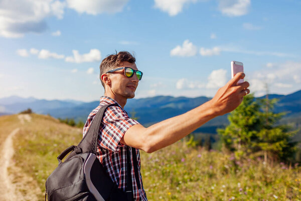 Man hiker taking selfie photo with smartphone in Carpathian mountains on hill peak. Traveler backpaker enjoys view of wild landscape