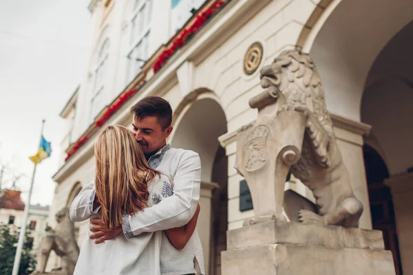 Happy couple in love walking in old Lviv city wearing traditional ukrainian shirts. Young people hug by town hall lion