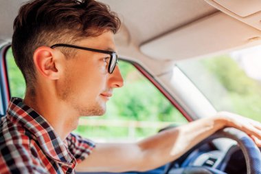 Direksiyonda el ele tutuşan gözlüklü genç adam. Şoför yola bakıyor. Adam otomatikle seyahat ediyor