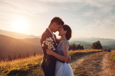 Mutlu çift gün batımında dağlarda sarılırken. Yazın Karpatlar 'da genç gelin ve damadın portresi.