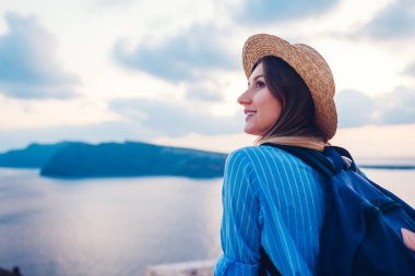 Yunanistan 'ın Santorini adasında yürüyen turist kadın gün batımında deniz manzarasına hayran. Sırt çantalı gezgin Oia 'da Caldera manzarasının tadını çıkarıyor