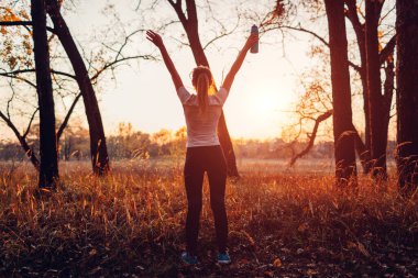 Koşucu antrenmandan sonra kollarını kaldırdı özgür ve mutlu hissederek eğitimde başarılı oldu. Sonbahar ormanlarında gün batımına hayran olan bir kadın. Sağlıklı yaşam tarzı
