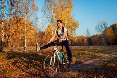 Sonbahar parkında bisiklet sürme egzersizi. Sonbahar ormanında bisiklete binen genç bir kadın bisikletçi bacak kaldırırken eğleniyor. Açık havada sağlıklı bir eğitim.