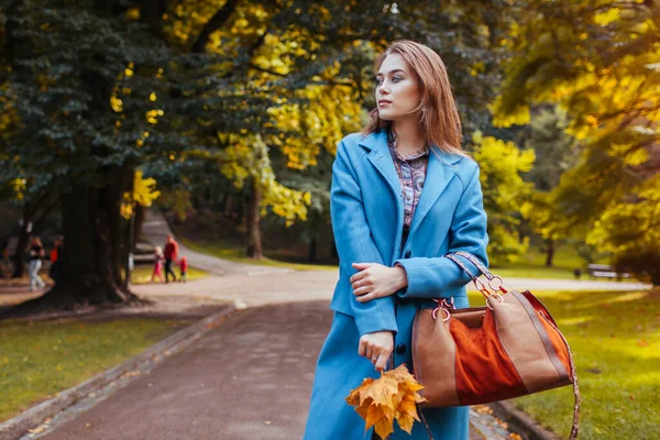 공원에서 핸드백과 나뭇잎을 여성의 아가씨는 유행하는 코트를 입는다 — 스톡 사진