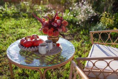 Sonbahar bahçesinde kahve ve bir buket güz çiçeğiyle kahvaltı. Bahçe mobilyaları balkabağıyla süslenmiş. İki kişilik sıcak içecek.