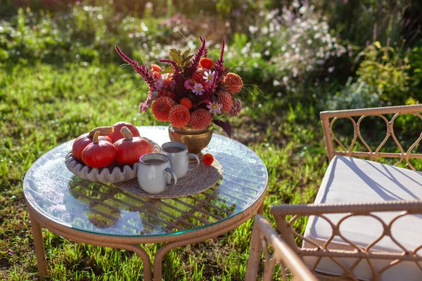 Sonbahar bahçesinde kahve ve bir buket güz çiçeğiyle kahvaltı. Bahçe mobilyaları balkabağıyla süslenmiş. İki kişilik sıcak içecek.