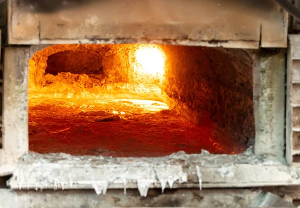 looking inside an aluminum melting furnace, in a foundry, with liquid metal and the oxidize dross layer on it