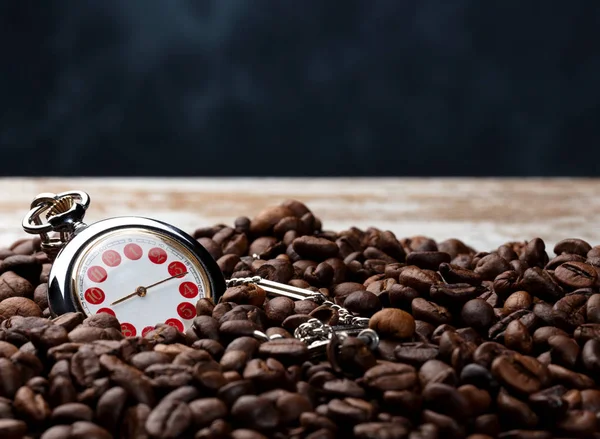 a lot of coffee beans with a hand watch on a worn brown wooden table and blue background, coceptual photo indicating that it is time for a good coffee