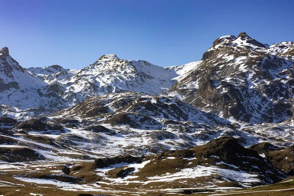 snowy mountains landscape showing the first snow on brown grass during the winter with a blue and clear sky