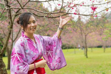 Asyalı kadın altında kiraz ağacı ve Sakura tanıtmak ve bu fotoğraf için ellerini yukarı kaldır. Kiraz çiçeği ile memnun olduğunu.