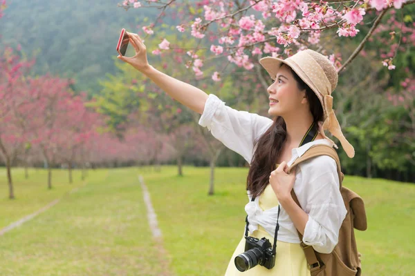 Kiraz ağacı altında duran ve bir selfie ile onların akıllı telefon alarak Asyalı Genç kız.