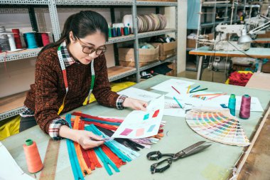 Yeni tasarım projesi için uygun fermuar seçmek için Asya Tasarımcısı masasında oturuyor. O stüdyoda çalışıyor.