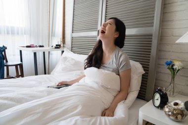 Asyalı kadın oturup yatak ve heyecan ile televizyon izlerken. O gülümseme ile memnun ve stresle bırakın. O komik sahne gördüm iken o delice kahkaha patladı.