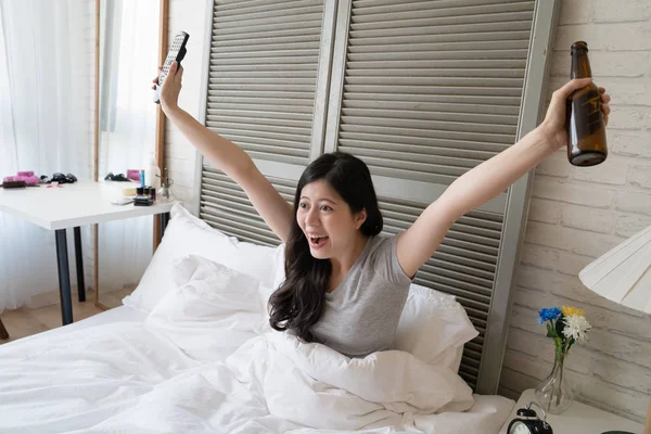 Asyalı kadın yan görünüm ellerini kaldırdı ve televizyon kazanan için bağırdı. Rock yıldızı göstermek için şaşkın olduğunu.