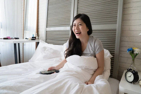 Asyalı kadın oturup yatak ve heyecan ile televizyon izlerken. O gülümseme ile memnun ve stresle yayın.