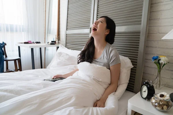 Asyalı kadın oturup yatak ve heyecan ile televizyon izlerken. O gülümseme ile memnun ve stresle bırakın. O komik sahne gördüm iken o delice kahkaha patladı.