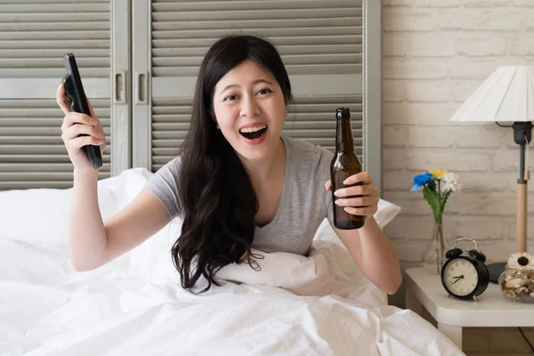 Asyalı kadın uzaktan kumanda ve bira şişesi onun elinde tutan. Onun en sevdiğim beyzbol oyuncusu için bir zafer zafer için çok neşeli kız.