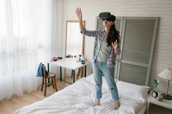 Asyalı kadın Vr aygıt gibi o kapma ve bir şey gerçek dünya yakalamak gibi havada kollarını germe yatağında oynarken.