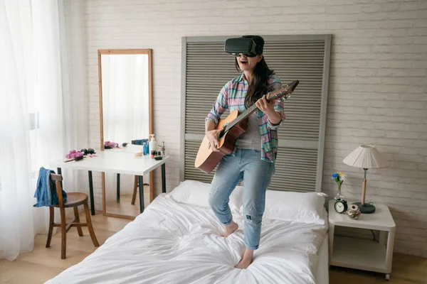 Asyalı kadın müzisyen yatağında ahşap gitar çalmak ve Vr giyiyor. O onun Vr aygıt onu beceri ile sosyal web sitesinde hayranlarıyla paylaşmak için kullanılan bir.