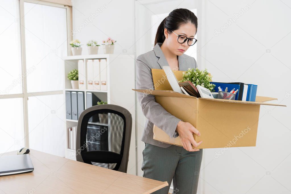 Asian woman packing and cleaning her office since she is going tho leave the company and resign. She is sad and reluctant to go away.