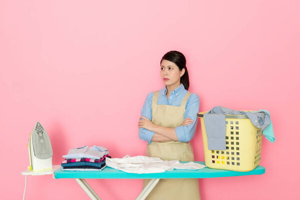 angry housewife unhappy to do housework standing behind ironing board