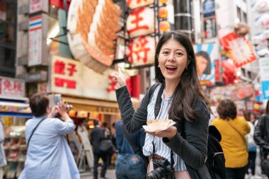 Asyalı kadın Simgesel Yapı Japonya ziyaret etti. dükkan için işaret ve hoş gülüyor.