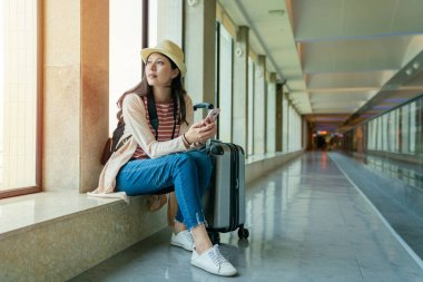 Asyalı kadın üstünde belgili tanımlık pencere oturuyordu. belgili tanımlık hareket eden holding. Havaalanı görünümünde.