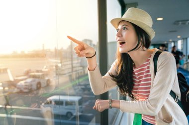 büyük pencerelerde eğilerek Asya ziyaretçi. duygu neşeli ve işaretleme bir yere at. Yarım vücut görünümü.