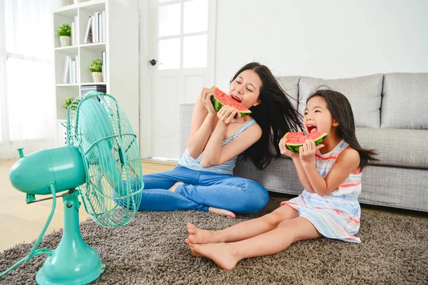 アジアのお母さんと女の子一緒にスイカを食べるします 電動ファンを吹いて自分の顔 楽しく素敵な時間をお楽しみください — ストック写真