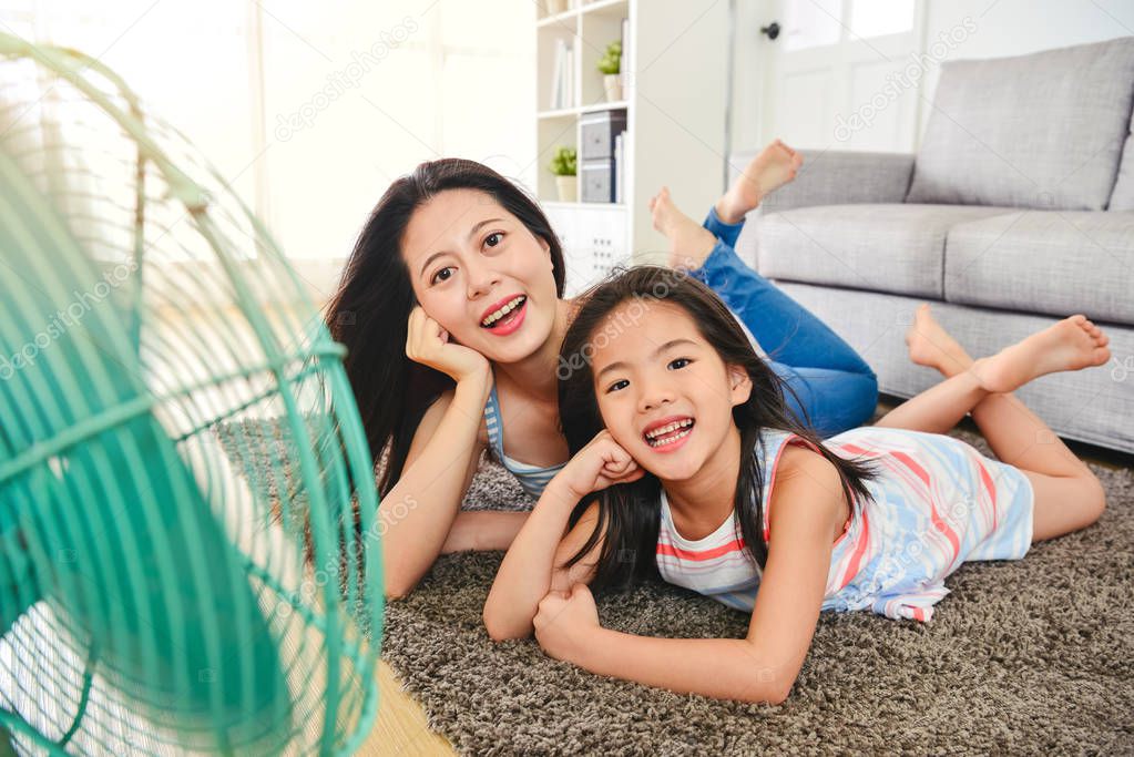 happy asian mom and kid cooling faces by fan. laughing and lying on the floor pleasantly. view from the full body at front.