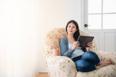 Genç güzel tablet kullanırken oturma odasında rahat bir kanepede oturan ve evde tüyler ürpertici aisan kız.