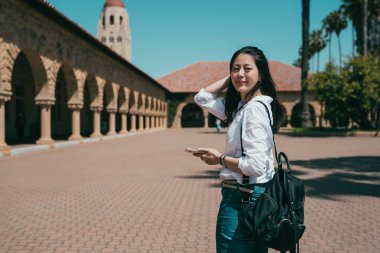 attractive asian exchange student holding a smartphone and turning around with a big smile. clipart