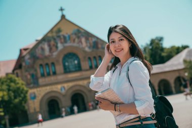 a beautiful asian student holding her books and looking into the camera with a charming smile. clipart