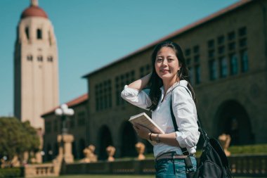 smart and beautiful asian student holding her book and visiting her dream university. clipart