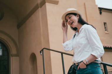 büyüleyici bir Asyalı kadın mutlu bir şekilde gülerek şapkasını tutarak yukarı doğru görünümünü.