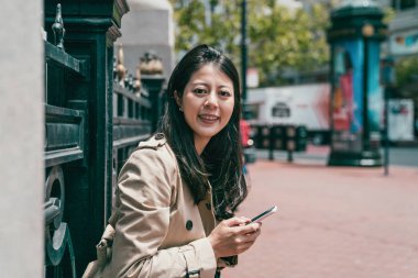 Kameraya gülümseyen ve kapıda bekleyen smartphone tutan güzel genç kadın.