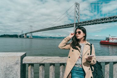 onun güneş gözlüğü bir cep telefonu ile bakarak düzenlenen diğer elinde tutarken genç zarif kadın.