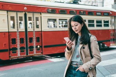 telefonunu tarama ve şehirde geçen trenin arka tarafından ayakta çekici genç kadın.