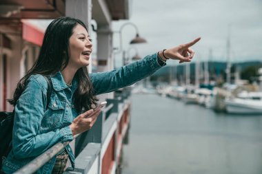 önde bir yere işaret ve heyecan verici telefonunu kullanırken gülüyor genç güzel kadın.