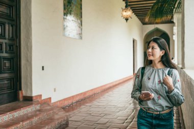 cep telefonu kullanırken tarihi bir binanın koridorda yürüyen bir genç güzel kadın.