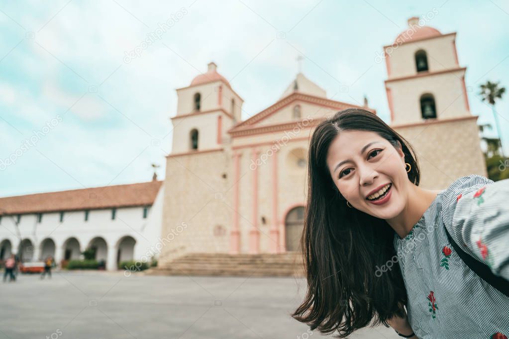 pretty and classy woman smiling and taking selfies joyfully with a stunning architecture.