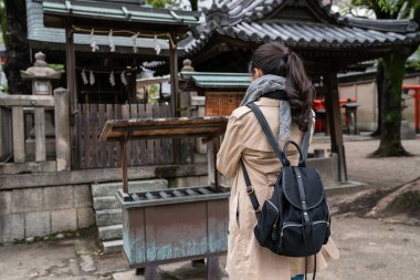 Arkadan Görünüş Japon kadının ailesi için dua. eşarp ve ağır bir sırt çantası taşıyan