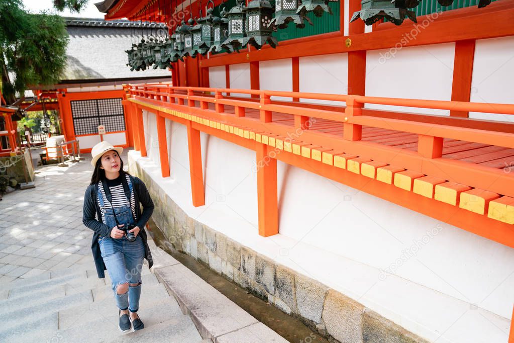 a full length photo of a confident female photographer joyfully walking up the stairs in the temple