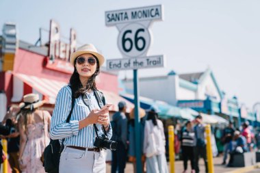 zarif bir kadın turist Santa Monica işaret yanındaki daimi harita kontrol cep telefonu kullanarak
