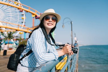 neşeli bir kadın fotoğrafçı ayakta eğlence parkı ve mavi okyanusun alarak fotoğraf