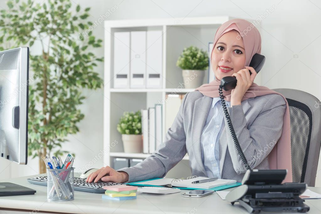 Muslim operator in office suit answering the phone call and face to camera smiling confidently. Businesswoman on telephone lifestyle.
