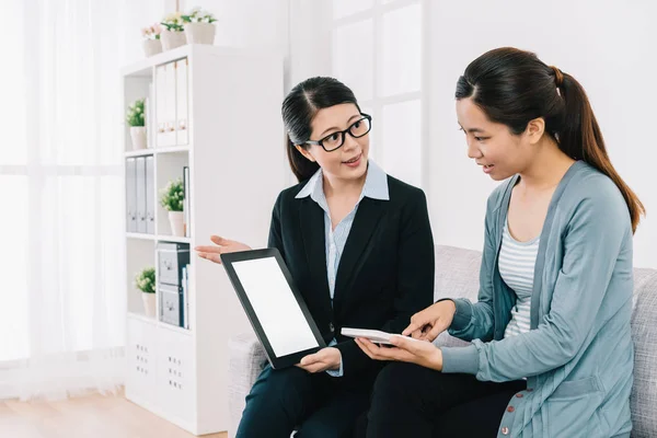 insurance advisor showing the insurance plan by digital tablet. housewife is counting the total payment by herself. two young ladies talking about their cooperation at home.