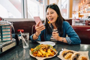 güzel kadın lokantada yemek ve yemek yerken smartphone tarafından bazı komik videoları izlerken rahatlatıcı. cep telefonunda oyun genç bayan. zarif kız çatal kullanarak.