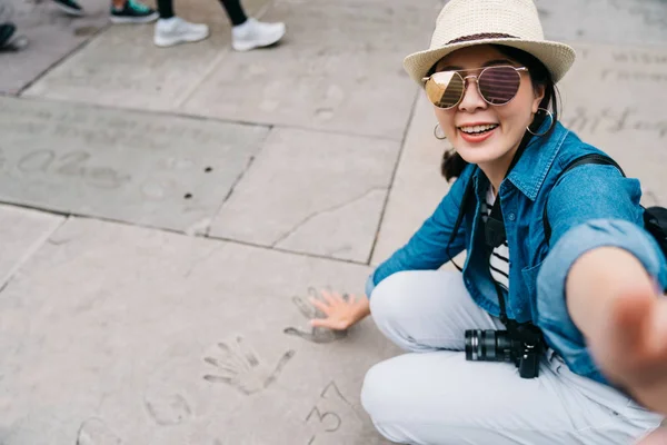 优雅的女性旅客蹲下来 并采取自拍与手掌标志在地面上 好莱坞大道上著名的星星手印 旅游美国夏季假日女孩享受城市 — 图库照片